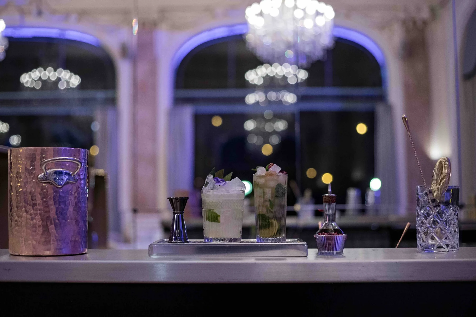Bar mobile L'Orchestre dressé dans un grand salon à lustre de cristal et fenêtres cintrées, ambiance bleutée du soir