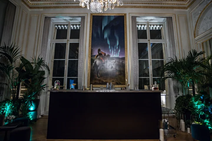Bar noir installé au centre d'un salon d'hôtel particulier : moulures, grand tableau, plantes éclairées en vert