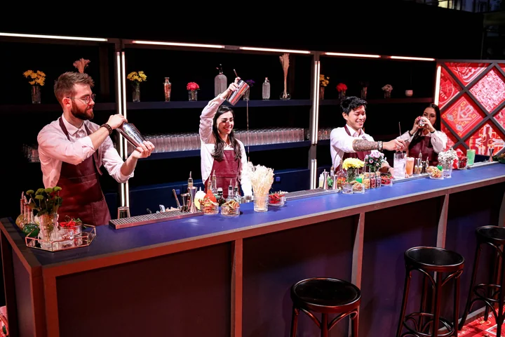 Long bar à l'éclairage rouge et bleu avec trois barmen en tablier bordeaux préparant des cocktails