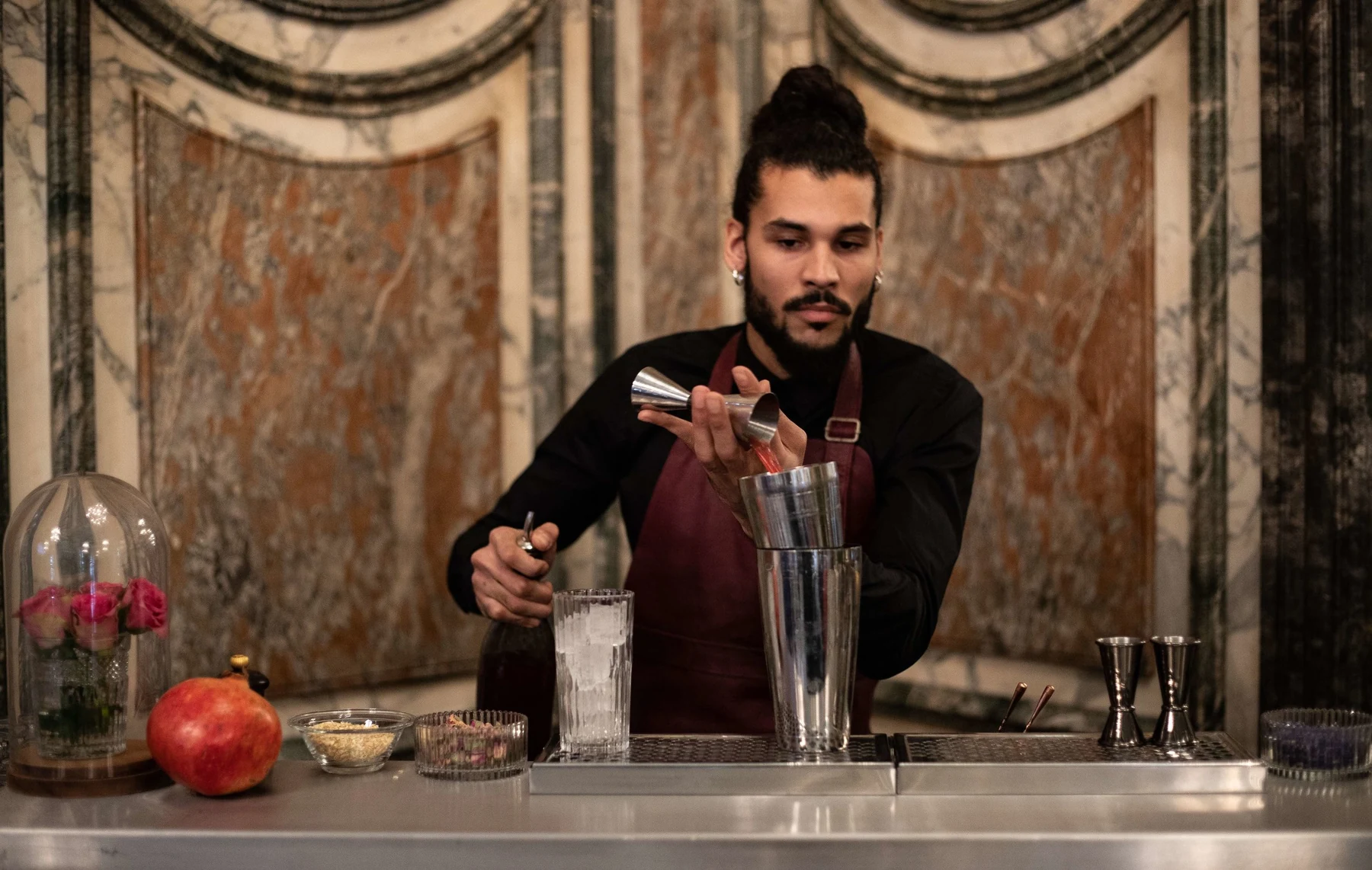 Barman au travail devant un mur de marbre ancien, grenade et cloche florale sur le comptoir