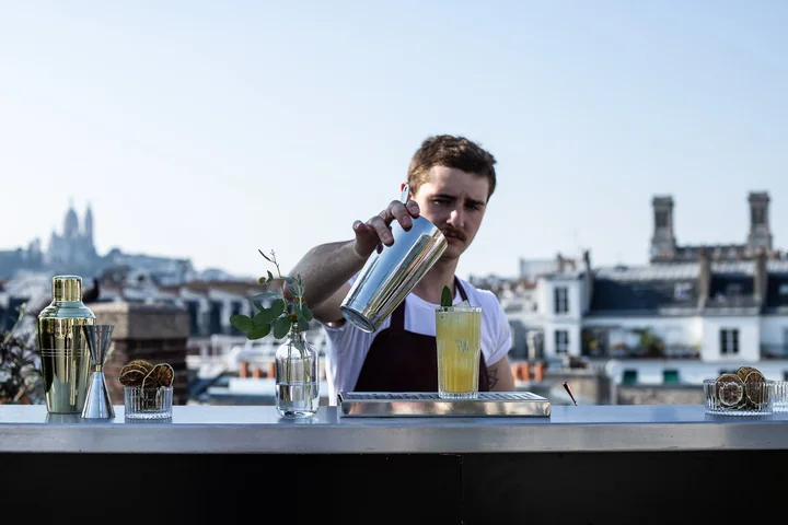 Barman servant un cocktail sur un rooftop parisien, vue sur les toits et le Sacré-Cœur en plein jour
