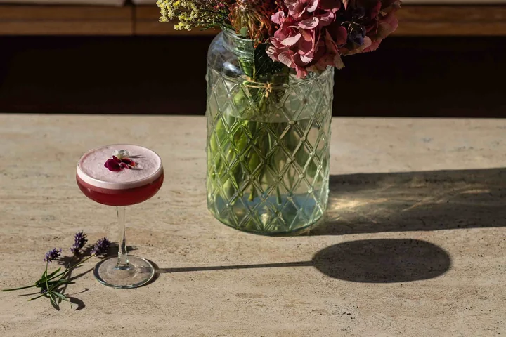 Coupe de cocktail rouge et vase de fleurs sur une table en pierre, ombres de plein soleil