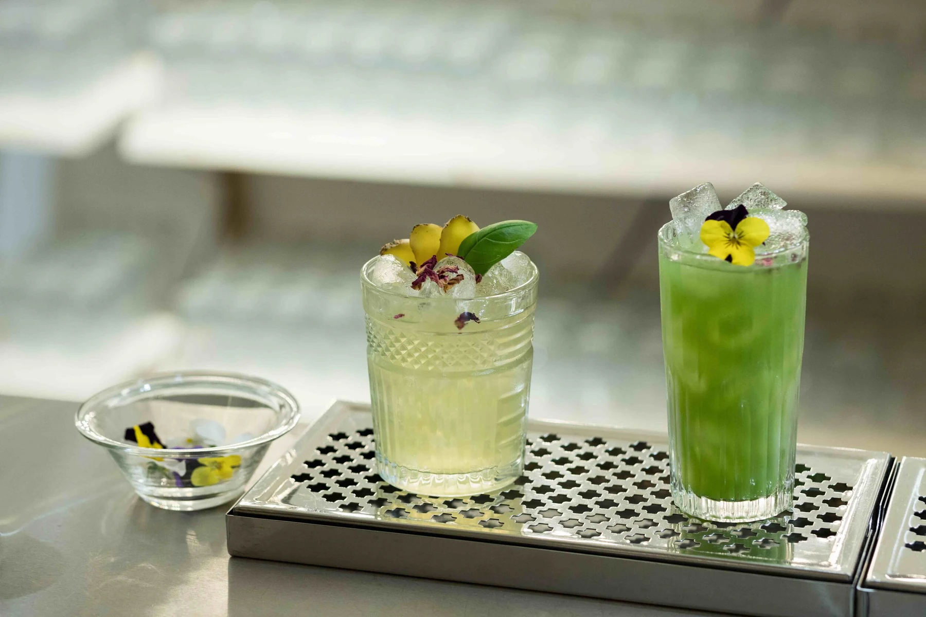 Deux cocktails verts garnis de fleurs comestibles sur égouttoir inox, lumière douce
